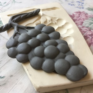 May include: A gray silicone mold for making a grape cluster. The mold is shaped like a bunch of grapes with a stem and leaves.