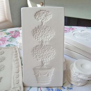 May include: White ceramic mold with a raised design of a three-tiered topiary tree in a pot. The mold is rectangular and has a smooth surface.