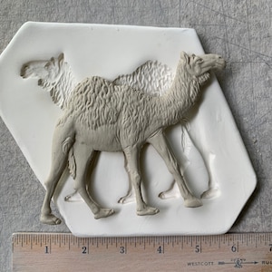 May include: A white silicone mold of two camels, one standing behind the other. The mold is approximately 6 inches long.