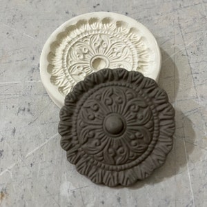 May include: A white silicone mold and a brown resin casting of a decorative round medallion with a floral design.