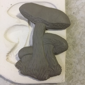 May include: A grey clay mushroom mould with two mushrooms, one on top of the other. The mould is made of silicone and has a smooth surface.