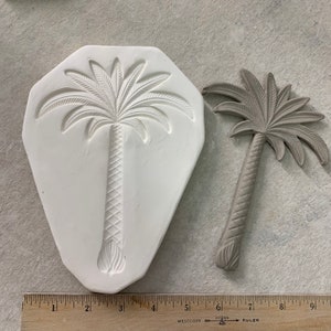 May include: A white silicone mold and a gray palm tree sculpture. The mold is shaped like a palm tree and has a detailed design. The sculpture is about 6 inches tall.