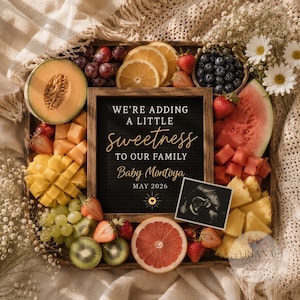 May include: A wooden letter board with the text WE'RE ADDING A LITTLE sweetness TO OUR FAMILY Baby Montoya MAY 2026, surrounded by fresh fruit including melon, grapes, strawberries, blueberries, mango, pineapple, grapefruit, and an ultrasound.