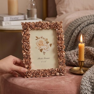 May include: A rectangular photo frame with a metallic copper finish, featuring a border decorated with sculpted three-dimensional roses. The frame contains an insert with a floral illustration and the text Photo Frame 4" x 6".