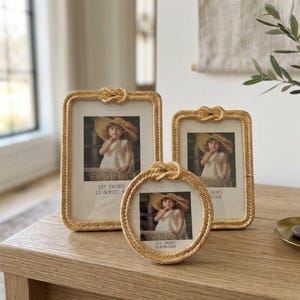 May include: Three gold-toned picture frames with a twisted rope texture and a decorative knot at the top. The set includes two rectangular frames and one circular frame, each containing a photograph of a child wearing a sun hat.