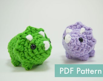 May include: Two crocheted amigurumi triceratops dinosaurs, one green and one purple, with black eyes and white horns.  PDF Pattern.