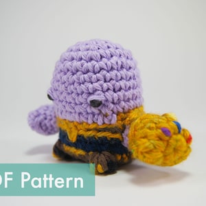 May include: Crocheted purple and yellow Thanos character with a gold infinity gauntlet. The character has a small, round body and a large head. The infinity gauntlet has six colorful gems.
