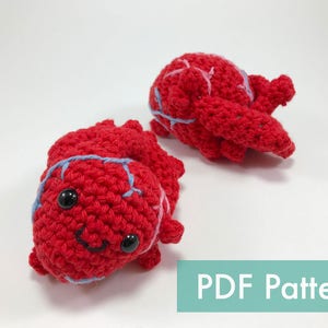 May include: Two handmade red crochet crab toys with black safety eyes and light blue accents. The crabs have a smiling face and are made with a textured stitch. The image also includes the text "PDF Pattern".