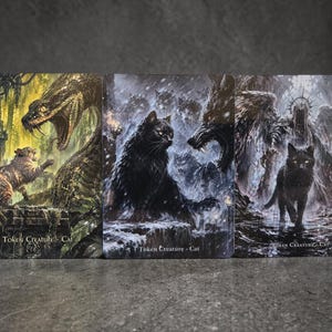 May include: Three fantasy art cards featuring cats. One card shows a cat facing a snake, another a black cat in a snowy scene, and the last a black cat with a dark angel. Each card has the text "Token Creature - Cat".