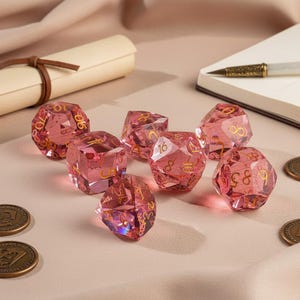 May include: A set of eight faceted, pink, polyhedral dice with gold numbering. The dice are arranged on a light pink surface, with a rolled parchment, a notebook, and coins in the background. The dice are for tabletop games.