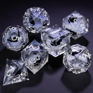 May include: A set of seven clear, multi-sided dice with a black cat silhouette design inside. The dice have white numbering and are designed for tabletop games. The dice are displayed on a dark surface.