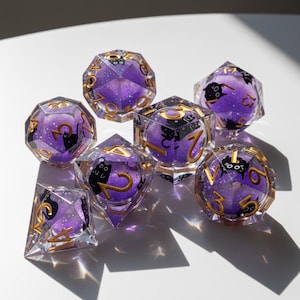 May include: Set of seven polyhedral dice with a purple and glittery interior. Each die features gold numbering and a black cat silhouette. The dice are made of clear resin and are designed for tabletop gaming.