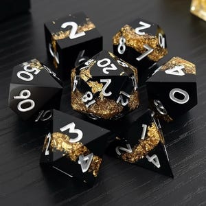 May include: Set of seven black polyhedral dice with gold leaf accents and white numbering. The dice are for role-playing games and include a D4, D6, D8, D10, D12, D20, and a percentile die.