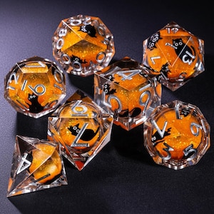 May include: Set of seven polyhedral dice with a Halloween theme. The dice are clear with orange glitter and black cat silhouettes inside. Each die has silver numbering. The dice are designed for tabletop games.