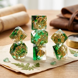 May include: A set of seven polyhedral dice with a green and gold color scheme. The dice are transparent with gold-colored numbers and intricate designs inside. The dice are arranged on a piece of parchment paper.