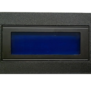 Puede incluir: Una pantalla electrónica negra rectangular con una pantalla azul. La pantalla está dentro de un marco negro texturizado con cuatro orificios de montaje. La pantalla es de color azul vibrante.