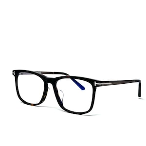 Peut inclure: Lunettes rectangulaires noires et écailles de tortue. Les lunettes ont un détail en métal foncé sur les branches et une teinte bleue sur les verres. Le fond est blanc.