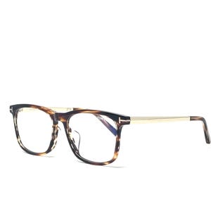 Op de afbeelding: Bril met een montuur met schildpadpatroon en goudkleurige veren. De rechthoekige monturen hebben een donkerbruin en zwart patroon. De veren zijn glanzend goudkleurig. De glazen zijn helder. De bril staat tegen een witte achtergrond.