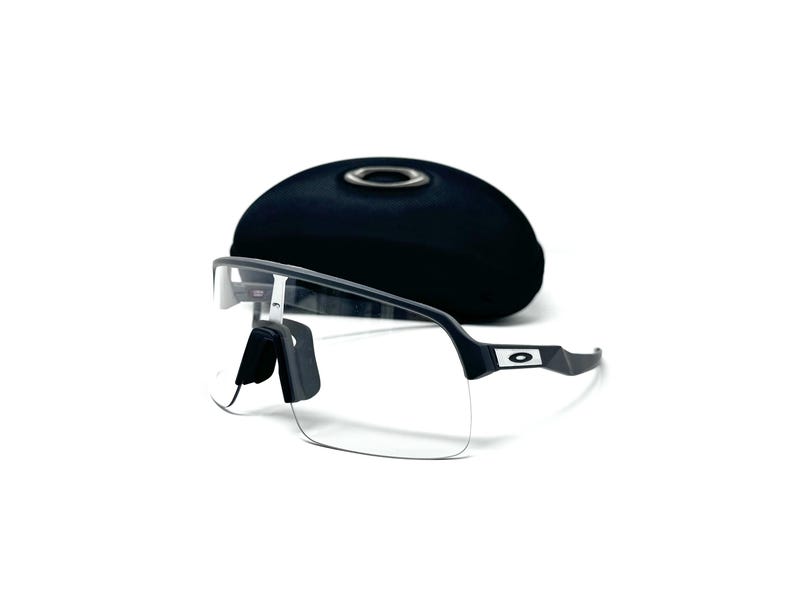 Op de afbeelding: Sportzonnebril met heldere glazen, zwart montuur en neuspads, voor een zwarte, ovale etui. De zonnebril heeft een modern design, geschikt voor buitenactiviteiten.