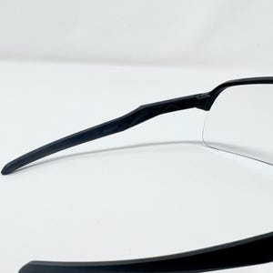 Op de afbeelding: Zwarte sportzonnebril met heldere glazen. De zonnebril heeft een strak, modern design met een zwart montuur en zwarte pootjes. De glazen zijn helder, in een wrap-around stijl, en bieden volledige bescherming.