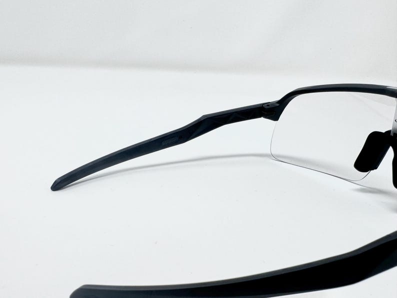Op de afbeelding: Zwarte sportzonnebril met heldere glazen. De zonnebril heeft een strak, modern design met een zwart montuur en zwarte pootjes. De glazen zijn helder, in een wrap-around stijl, en bieden volledige bescherming.