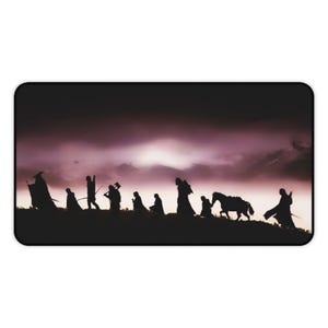 May include: A rectangular desk mat featuring a dark silhouette of a group of nine figures, including one on horseback, walking across a ridge against a dramatic, cloudy purple and black sky. The scene depicts a line of travelers in profile.