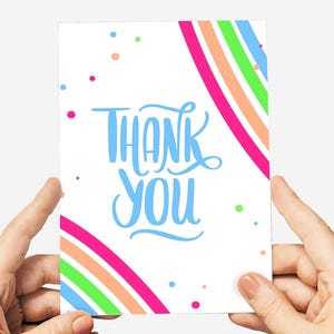 May include: A white card with the words "THANK YOU" in blue script. The card has a rainbow design with pink, orange, green, and blue stripes. Small colorful dots are scattered around the card.