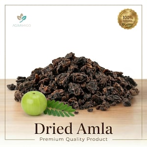 Puede incluir: Un montón de bayas de amla secas de color marrón oscuro, una fruta de amla verde y una ramita de hojas. El texto "Dried Amla" y "Premium Quality Product" se muestran debajo. Un sello dorado dice "100% Natural".
