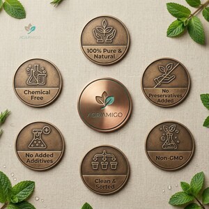 May include: A collection of bronze-colored circular medallions with embossed text and icons, including "100% Pure & Natural", "Chemical Free", "No Preservatives Added", "No Added Additives", "Clean & Sorted", and "Non-GMO". The central medallion features the brand name "AGRIAMIGO". Fresh mint sprigs are scattered around the medallions.