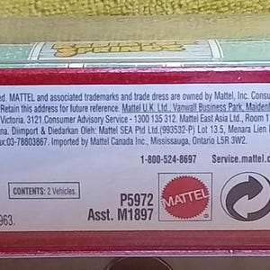 May include: A red and green packaged toy car. The packaging includes the text "MADE IN CHINA", "MATTEL", and a barcode. The package also includes the text "CONFORMS TO THE SAFETY REQUIREMENTS OF ASTM F963".