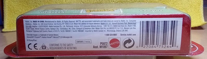 May include: A red and green packaged toy car. The packaging includes the text "MADE IN CHINA", "MATTEL", and a barcode. The package also includes the text "CONFORMS TO THE SAFETY REQUIREMENTS OF ASTM F963".