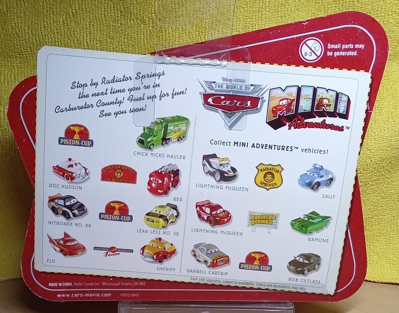 May include: A red and white package featuring various miniature toy cars from the "Cars" movie franchise. The package includes images of Lightning McQueen, Sally, and other characters. Text on the package reads "Collect MINI ADVENTURES vehicles!" and "Stop by Radiator Springs".