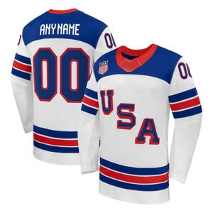 May include: White hockey jersey with blue and red accents. The jersey features the text "USA" in red, the number "00" in red, and the name "ANYNAME" on the back. The jersey has long sleeves and a red collar.