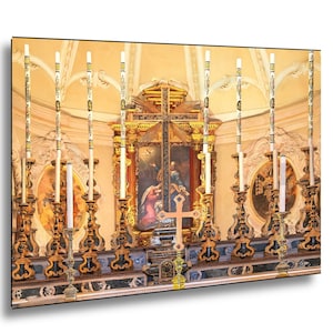 May include: An ornate church interior featuring a golden altar with a cross and a painting. Tall, decorated candles stand in front of the altar, and the ceiling is arched. The overall color scheme is warm, with gold, beige, and touches of blue.