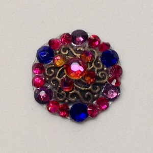May include: A decorative, round brooch with a bronze filigree center, surrounded by vibrant, colorful rhinestones. The rhinestones are in shades of red, pink, blue, and orange, creating a sparkling, eye-catching design. This brooch is perfect for adding a touch of glamour.