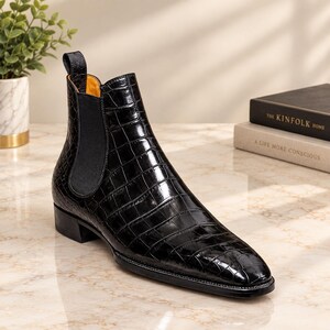 Può includere: Uno stivaletto Chelsea nero con tomaia in pelle lucida stampa coccodrillo, punta affusolata, inserto elastico laterale nero, linguetta sul tallone e fodera interna giallo brillante. Lo stivale presenta un tacco basso e una suola nera liscia.