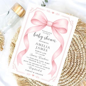 Puede incluir: Una tarjeta de invitación rectangular para baby shower con un gran lazo de cinta rosa estilo acuarela en la parte superior. El texto dice: Please join us for a baby shower honoring Amelia James, March 20th at 11:00 AM, James Residence, 123 Pink Bow Lane, Baby Shower Way, 55555, RSVP to Amanda by March 12th on 0000000000, Registered at Target & Amazon.