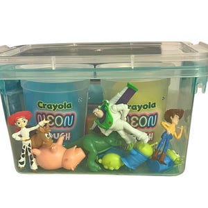 May include: A clear plastic container with a teal rim and lid, filled with Crayola Neon Dough and Toy Story character figurines. The container holds blue and yellow dough tubs, and various character toys.