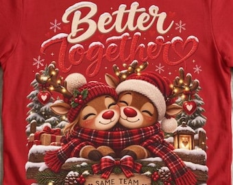 May include: A red short-sleeve t-shirt featuring a graphic of two reindeer wearing hats and scarves, huddled together. The text reads Better together and SAME TEAM ALL SEASON. The design includes pine trees, gifts, and snowflakes in a festive style.