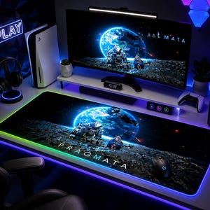May include: A gaming setup featuring a large black mousepad with a space-themed graphic and the word "PRAGMATA". A computer monitor displays a similar image. Other items include a gaming console, headphones, and a neon "PLAY" sign.