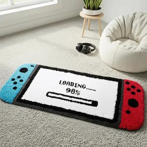 Peut inclure: Un tapis touffeté rectangulaire en forme de console de jeu portable. Le centre présente un écran blanc avec le texte noir LOADING... 98% et une barre de progression. Le côté gauche est bleu et le droit est rouge, avec des boutons noirs.