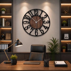 Puede incluir: Un reloj de pared grande y redondo con un marco de metal negro y un centro de madera. El reloj presenta números negros grandes y estilizados y manecillas blancas. El reloj está montado en una pared de color neutro en un entorno de oficina bien iluminado.