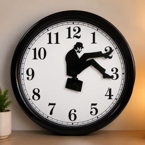 May include: Black and white wall clock with a unique design. The clock face is white with black numbers and a black border. The clock hands are replaced with a black silhouette of a man with a briefcase, sitting on the clock face.