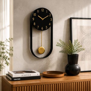 May include: A wall clock featuring a circular black face with gold-coloured numerals and hands. The clock is suspended within a black oval frame and includes a gold-coloured pendulum that hangs below the clock face, creating a vertical design.