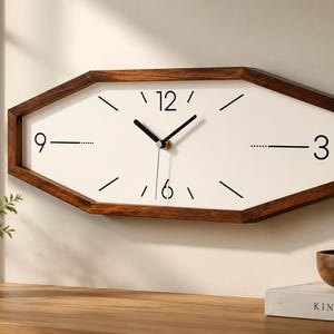 May include: A modern, geometric wall clock with a white face and dark brown wooden frame. The clock features black hands and hour markers at 12, 3, 6, and 9. The clock's dimensions are approximately 18 inches wide.