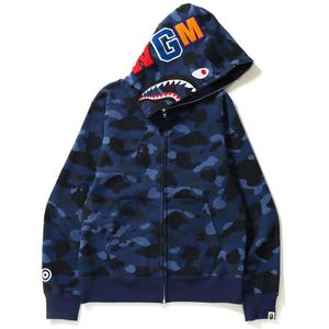 May include: A blue camouflage zip-up hoodie with a hood featuring the letters "MGM" in orange and blue. The hood has a shark mouth design. The hoodie has a front zipper and two pockets.