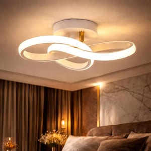 Op de afbeelding: Moderne witte plafondlamp met een uniek, verweven lusontwerp. Het licht straalt een warme, uitnodigende gloed uit, perfect voor slaapkamers of woonruimtes. De armatuur is gemonteerd op een witte basis met een goudkleurige centrale steun.