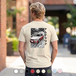 Può includere: T-shirt beige con grafica di un'auto rossa e bianca che sbanda su una strada, con testo giapponese. Il disegno è in una cornice rettangolare nera. La maglietta è a girocollo.