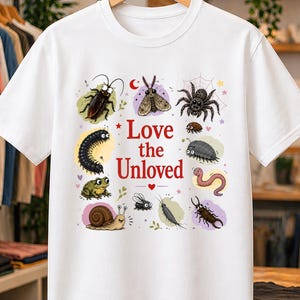 Op de afbeelding: Een wit t-shirt met korte mouwen en een centrale afbeelding met de rode tekst Love the Unloved, omringd door illustraties van diverse insecten en kleine wezens zoals een spin, slak, kikker, worm en mot op kleurrijke vlakken.