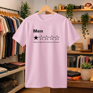 May include: A light pink short-sleeved t-shirt featuring the black text 'Men' above a graphic of five stars, with only the first star filled in black. Below the stars, the text reads 'Absolute nightmares, would not recommend.'